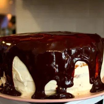 A close-up of a whole vanilla cake with melted chocolate icing. 