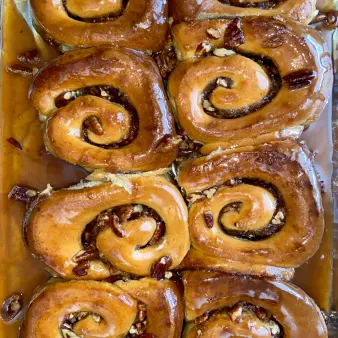 A close-up of sticky buns in a baking dish with glaze and pecans. 